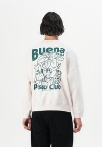 Lichtroze sweatshirt met een grote groene afbeelding op de achterkant met cartoon voedselkarakters en de tekst "Buena Pasta Pisto Club".