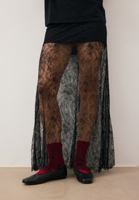 Czarna koronkowa spódnica z kwiatowym wzorem, półprzezroczysty materiał i boczne rozcięcia, zestawiona z czerwonymi skarpetkami i czarnymi balerinami. Prosty, elegancki design.
