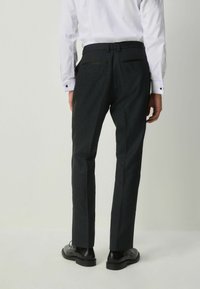 Fekete, finoman mintázott, szabott nadrág, lapos derékkal, hátsó zsebekkel és egyenes lábformával. Fényes fekete cipővel viselve.