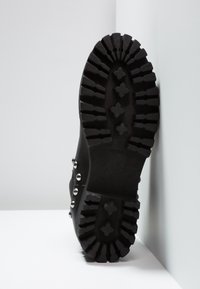 Botte noire avec une semelle en caoutchouc à crampons profonds pour une meilleure adhérence, ornée de clous argentés sur le côté, et un design robuste.