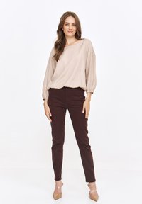 Beżowy, luźny top z marszczonymi rękawami, w połączeniu z dopasowanymi ciemno-brązowymi spodniami i cielistymi szpilkami. Prosty, teksturowany wzór.