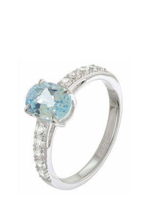 Silver ring with a large oval blue gemstone center and small round clear gems set along the band sides.