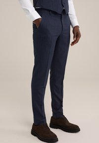 Pantalon ajusté bleu marine avec un discret léger fin rayé, fabriqué à partir d'un tissu texturé. Il présente des poches latérales et une coupe slim, associé à des chaussures brunes.