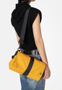 Borsa a spalla gialla in nylon con tracolla nera, design a soprarollo e dettaglio del logo. Texture liscia e hardware robusto per una chiusura sicura.