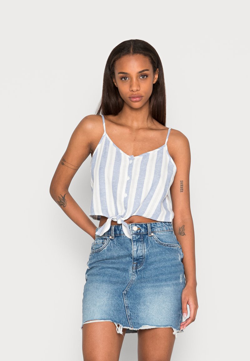 Top cropped listrado azul e branco com detalhe de nó na frente, combinado com uma saia mini de denim de cintura alta com bainha desfiada.