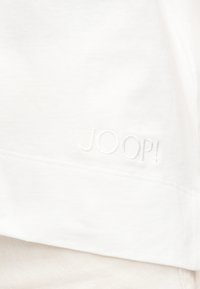 Λευκό ύφασμα με διακριτική ανάγλυφη κεντητική της λέξης "JOOP!" κοντά σε μια ραμμένη ραφή.