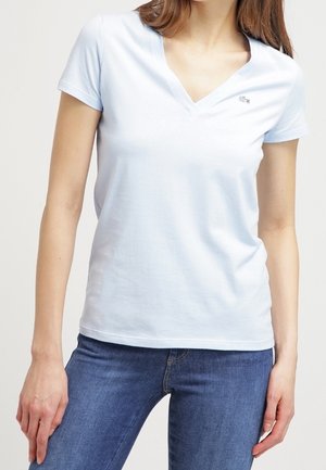 T-shirt bleu clair à manches courtes et col en V, en coton doux. Présente un petit logo sur la poitrine et une coupe décontractée.