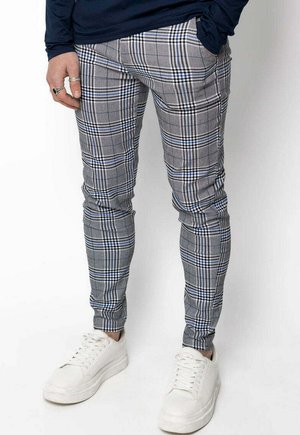 Pantalon à carreaux gris avec des lignes bleues et blanches, design ajusté et texture lisse, associé à des baskets blanches pour le contraste.