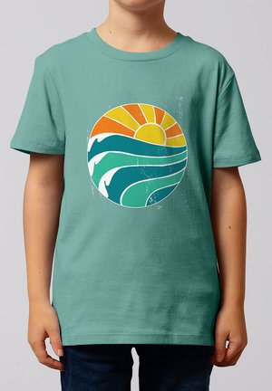 Kind trägt ein türkises Hemd mit einem kreisförmigen Motiv einer stilisierten Sonne und Ozeanwellen in Orange, Gelb, Weiß und verschiedenen Blautönen.