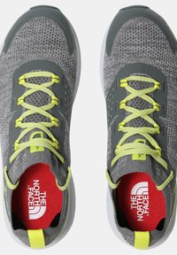 Zapatillas deportivas grises con una parte superior de malla texturizada, acentos en amarillo neón y una suela de goma blanca. En el interior presentan una plantilla roja con marca.