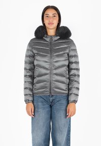Giacca puffera grigia con colletto soffice, caratterizzata da un design a righe orizzontali, chiusura con zip frontale e polsini elasticizzati. Abbinata a jeans a gamba larga.