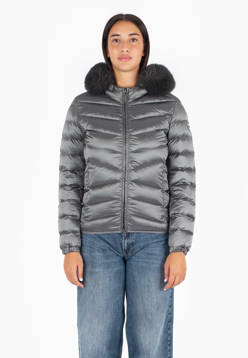 Giacca puffera grigia con colletto soffice, caratterizzata da un design a righe orizzontali, chiusura con zip frontale e polsini elasticizzati. Abbinata a jeans a gamba larga.