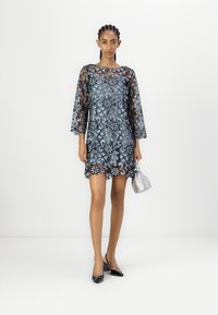 Spetsklänning med blommönster i blå och svarta nyanser, trekvartslånga ärmar, vågig nederkant, kombinerad med en silverhandväska och svarta klackar.