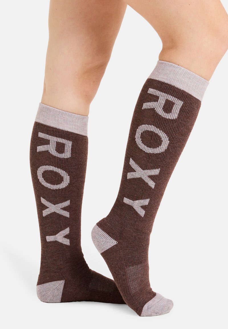 Brązowe skarpetki do kolan z jasnoszarym napisem „ROXY”. Posiadają ribbowaną teksturę oraz kontrastujące jasnoszare akcenty w okolicy mankietu i pięty.