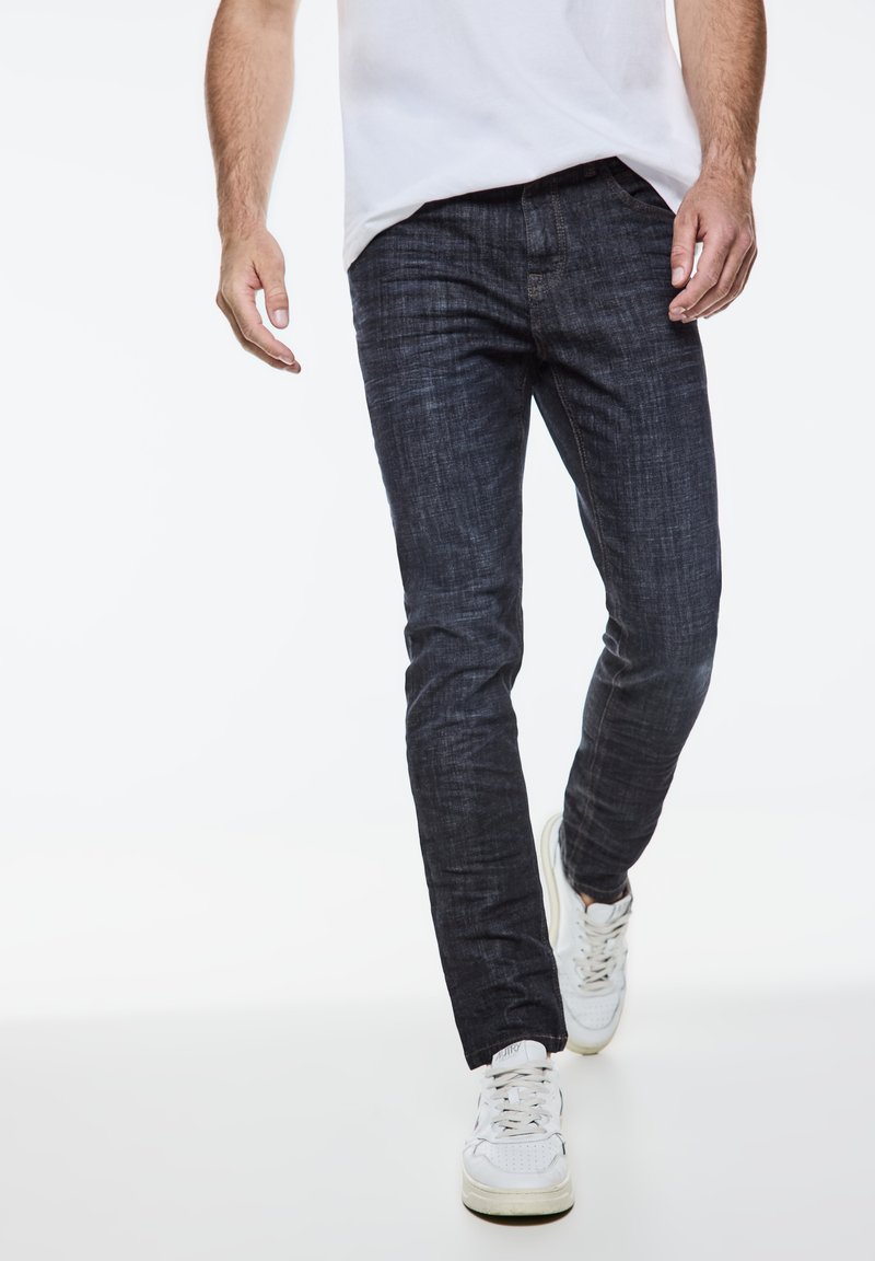 Mörka denimjeans med tapered passform; har en subtil textur och femficksdesign, parat med vita sportskor.