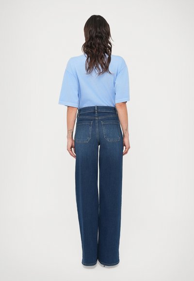 Sötétkék, széles szárú farmernadrág, magas derékkal, hátul zsebekkel és sima textúrával. Világoskék, túlméretezett pólóval párosítva.