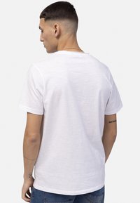T-shirt blanc à manches courtes en tissu léger, présentant un col rond et une coupe décontractée, avec une texture lisse.