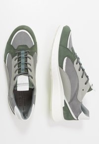 Scarpe sportive grigie e verdi realizzate in camoscio e mesh, dotate di punta tonda, dettagli bianchi e una suola spessa bianca.