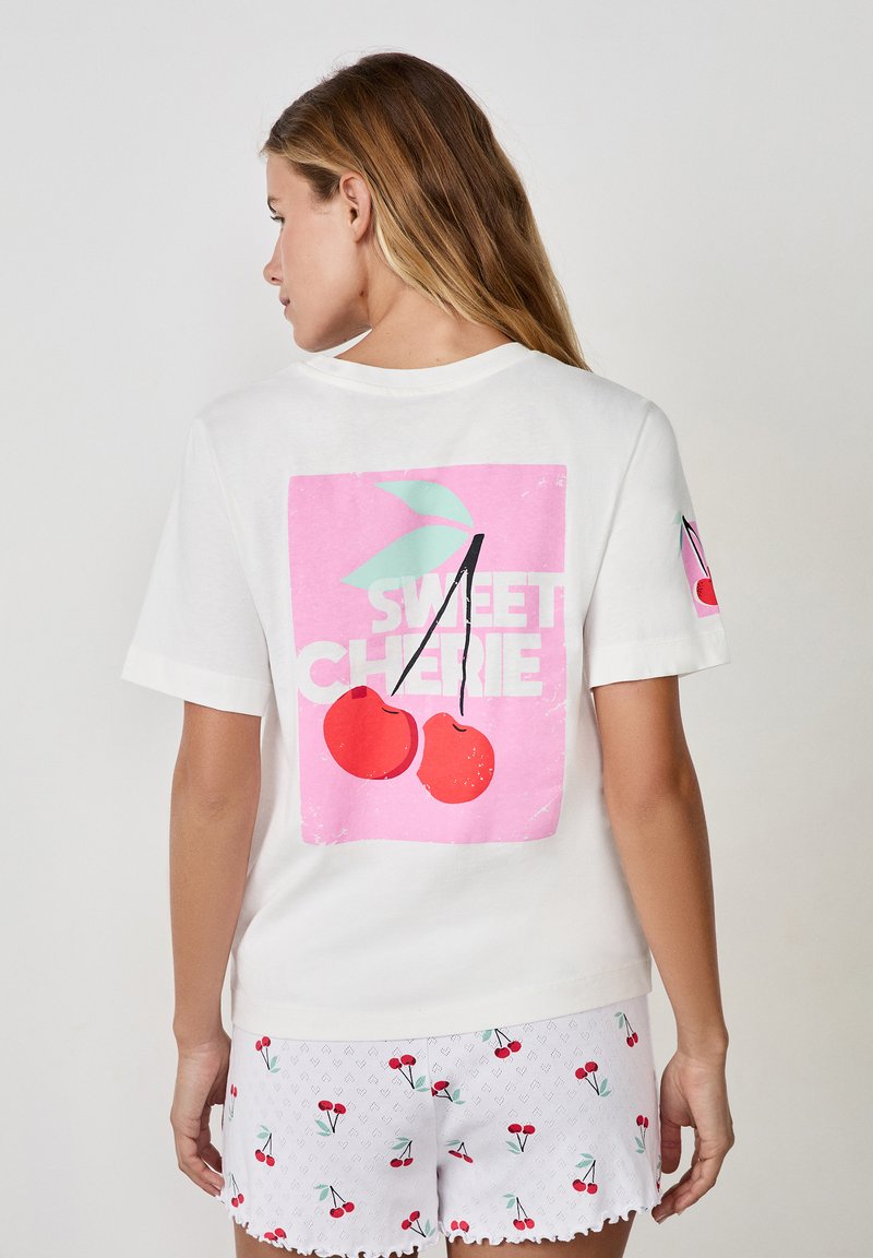 Biała koszulka z różową grafiką przedstawiającą wiśnie oraz napisem "SWEET CHERIE" na plecach, krótki rękaw, luźny krój.