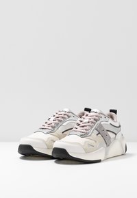 Zapatillas ligeras con una combinación de materiales beige, gris y rosa. Presentan texturas de malla y sintéticas, punta redondeada y una suela negra.