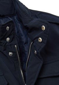 Giacca blu navy con collo strutturato, bottoni a pressione argentati e cerniera frontale. Presenta una morbida fodera interna e un tessuto leggermente testurizzato.