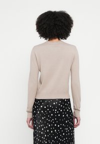 Bēša džemperis ar apaļu izgriezumu un garām piedurknēm, ar ribotu aproču un apakšmalu. Kombinēts ar melnu svārku ar baltām polka punktu rotājumiem.