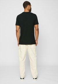 Black cotton t-shirt with a classic round neckline, short sleeves, paired with cream-colored cargo pants featuring side pockets.