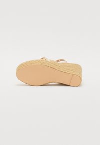 Sandalia de cuña de esparto con diseño de cuerda de yute, parte superior beige y suela de goma lisa. Presenta tiras ajustables para un ajuste seguro.