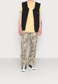 Black sleeveless vest over a yellow T-shirt, paired with beige camouflage cargo pants and black sneakers with white soles.