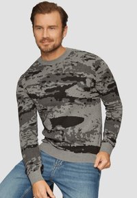 Pull en laine gris avec un motif camouflage noir, encolure ronde et poignets et ourlet côtelés. Porté sur un jean bleu.