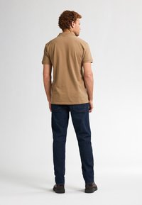 Polo marrón de manga corta, combinado con unos vaqueros azul oscuro. La camisa cuenta con un cuello clásico y un ajuste relajado. Footwear negro completa el look.