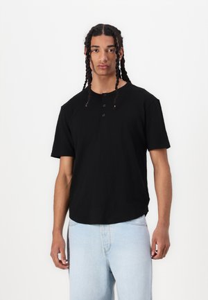 Black short-sleeve T-shirt with a round neckline and three buttons. Made of cotton, featuring a relaxed fit and subtle texture.