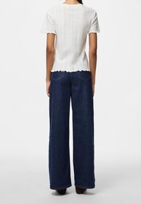 Vit ribbad topp med vågiga kanter, kombinerad med mörkblå vida jeans. Outfiten har en minimalistisk design med en avslappnad passform.