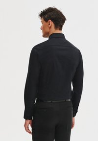 Ciemnoniebieska koszula z długim rękawem o strukturalnym kołnierzyku, teksturowanej tkaninie, dopasowanym kroju i zapinanych mankietach, zestawiona z czarnymi spodniami.