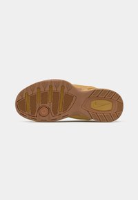 Zool van een mosterdgeel Nike sneaker met gestructureerde grippatronen en een zichtbare Nike swoosh op de hak.