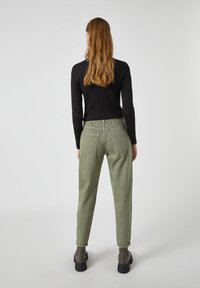 Top de manga larga negro de canalé combinado con pantalones holgados verdes oliva que presentan una cinturilla elástica y puños enrollados, usados con botas gris de tobillo.