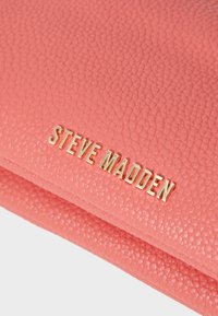 Pink pebbled leather clutch with a metallic gold "STEVE MADDEN" logo. Features a textured surface and folded design.