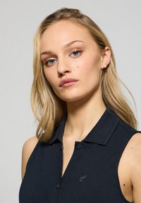 Polo shirt senza maniche di colore blu navy con colletto a bottoni, caratterizzato da un logo discreto e una texture a coste. Design semplice e classico.