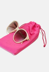 Γυαλιά ηλίου με ανοιχτόχρωμο καβούκι και καφέ φακούς, τοποθετημένα σε μια φωτεινή ροζ σακούλα με κορδόνι που έχει ανάγλυφο το "vogue eyewear".