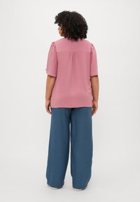 Light pink short-sleeve top with textured fabric and gathered shoulder detail, paired with loose-fitting blue trousers.