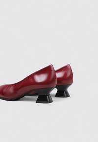 Escarpins en cuir rouge avec une finition brillante. Présentent un talon évasé bas en noir. Design à bout rond. Texture lisse avec une silhouette élégante.