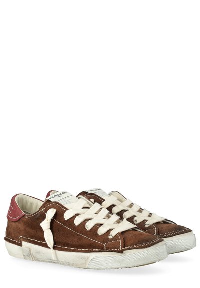 Sneaker in suede marrone con lacci bianchi, suole bianche e accenti rossi sul tallone, che mostrano piccoli segni di usura sulle suole.