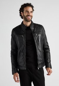 Zwarte leren jas met een opstaande kraag, twee ritszakken op de borst en een aansluitend ontwerp. Het oppervlak heeft een soepele textuur.