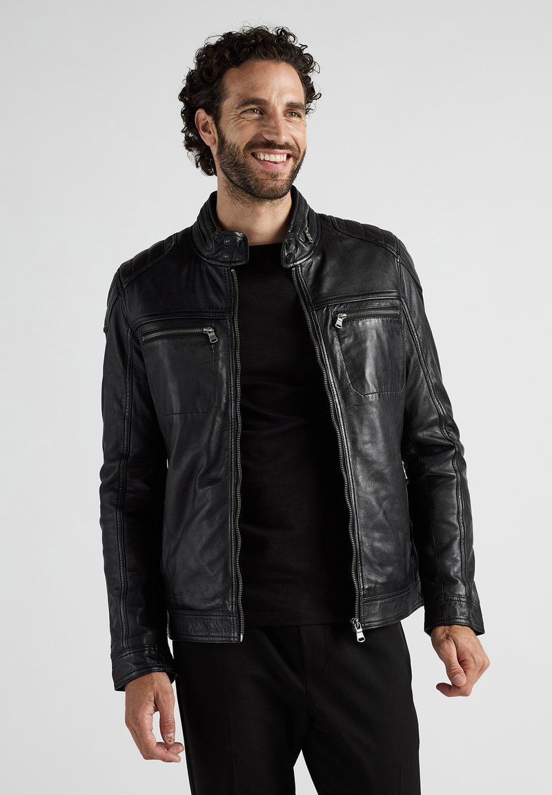 Zwarte leren jas met een opstaande kraag, twee ritszakken op de borst en een aansluitend ontwerp. Het oppervlak heeft een soepele textuur.