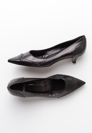 Černé kožené dámské lodičky s špičatou špičkou, dekorativním šitím podél okrajů a nízkým podpatkem typu kitten heel. Rovnoměrně hladká textura.