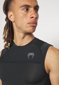 Black sleeveless athletic shirt with a fitted design, textured fabric, and a gray snake logo on the chest, highlighting performance features.