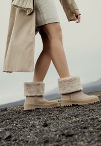 Botas de tobillo beige de ante con un suave puño de piel sintética, que cuentan con una suela de goma gruesa con agarre texturizado y un acento de logo minimalista.