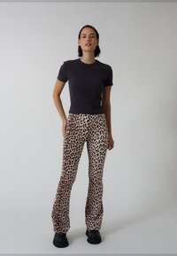 T-shirt noir moulant associé à un pantalon beige évasé avec un imprimé léopard marron, porté avec des bottes plateformes épaisses noires.