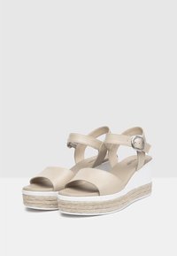 Beige leren wedge sandalen met kruislings banden en een zilveren gesp, met een jute-wrapped zool en een witte platformbasis.