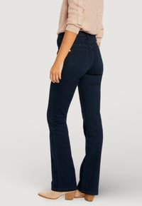 Jeans acampanados de mezclilla azul oscuro con cintura alta, con bolsillos traseros y costuras sutiles. Combinados con botines beige.